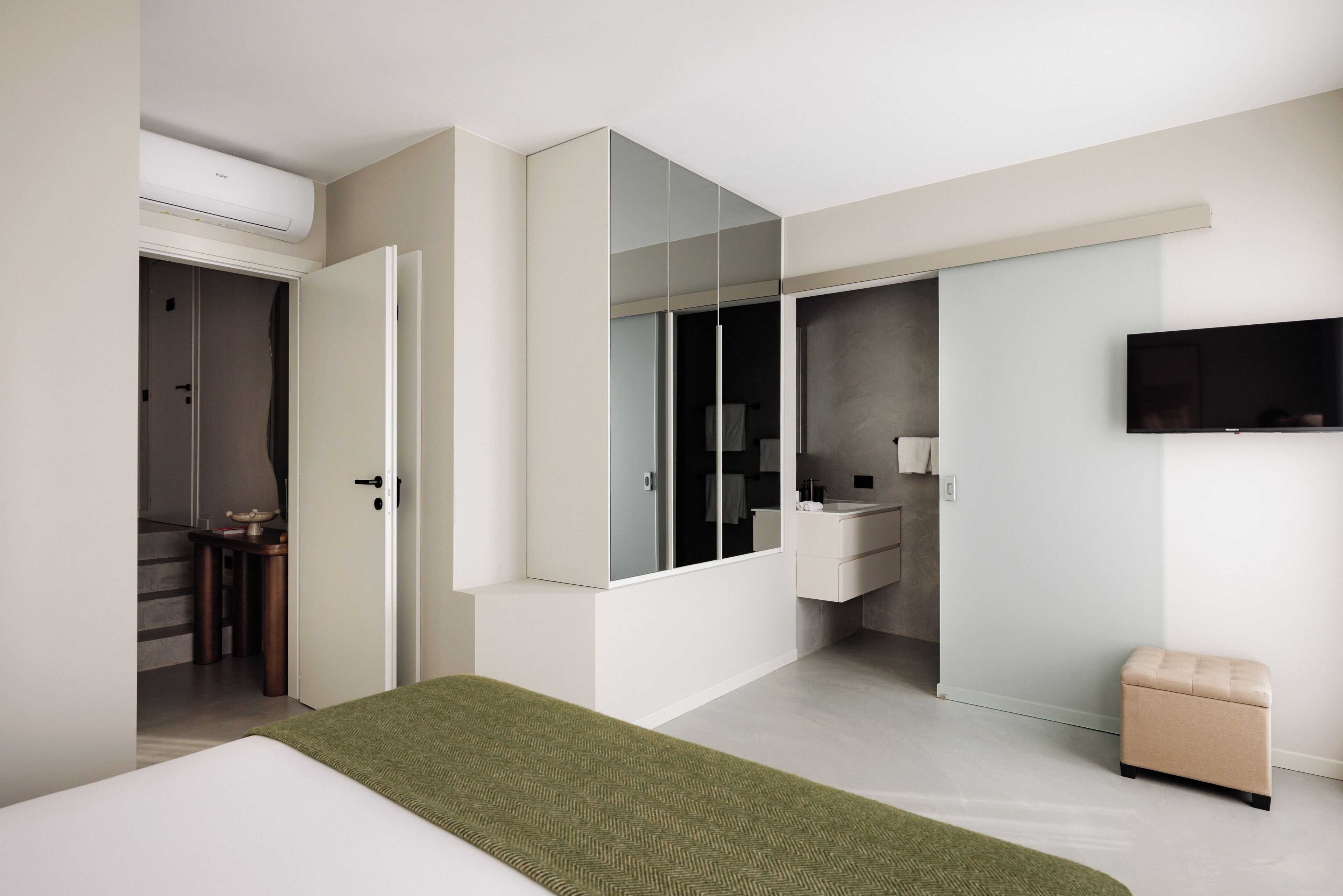 A modern bedroom with a bed, a green throw, a wardrobe, a vanity, and a television.