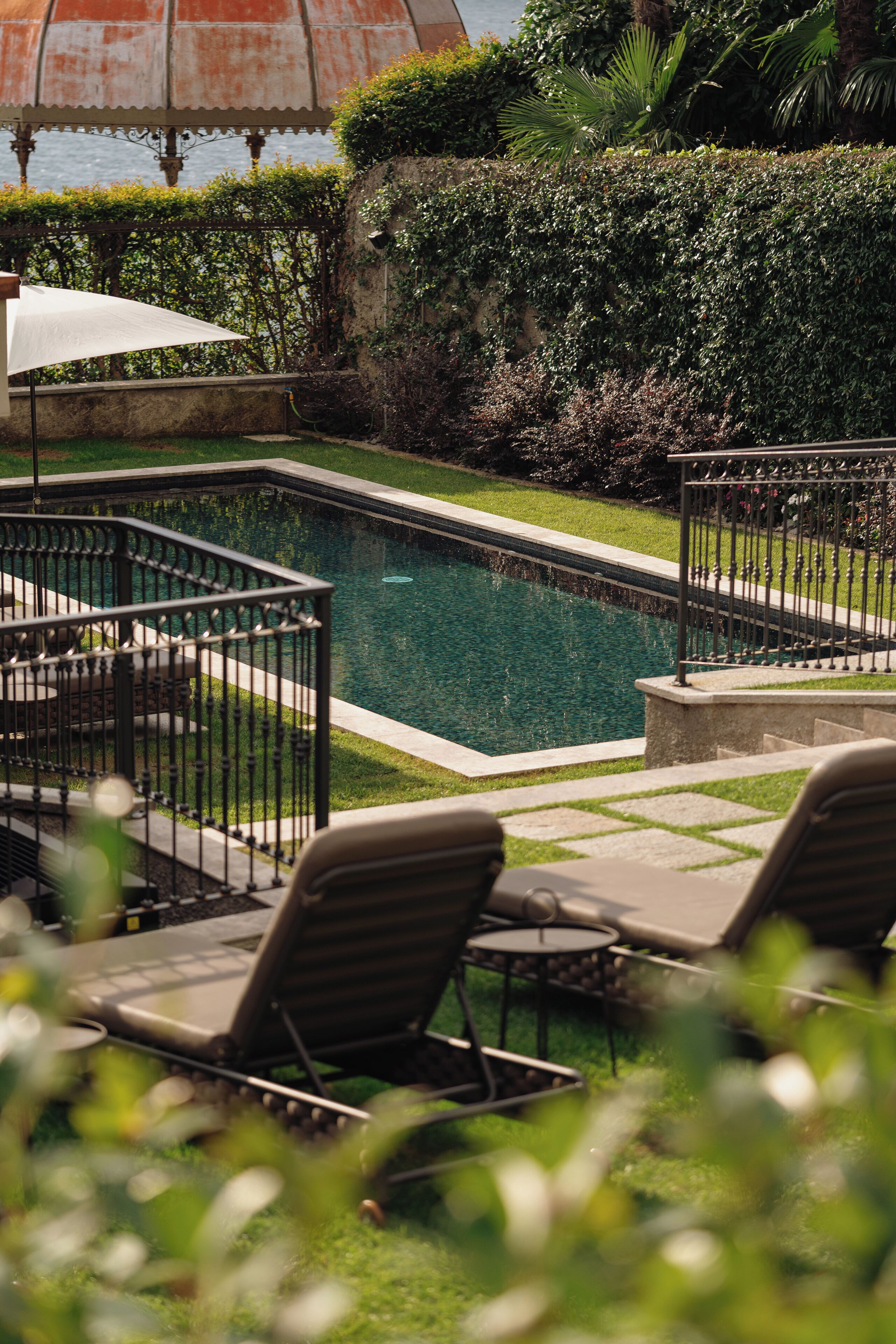 Una piscina circondata da un solarium, con poltrona prendisole e un pergolato con ombrellone.