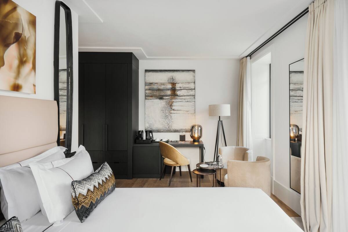 A hotel room with a large bed, a desk, a chair, a lamp, and artwork on the walls.