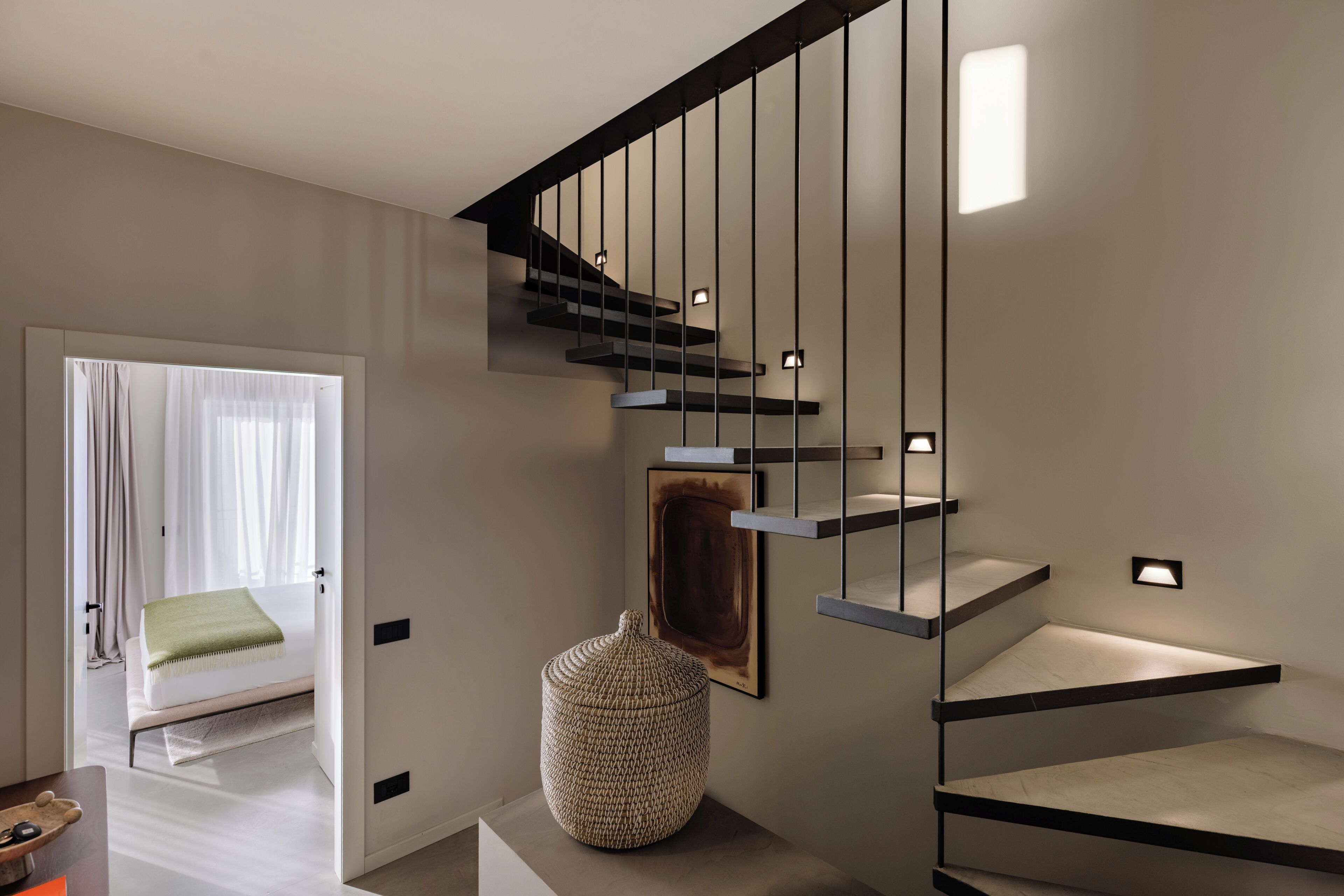 A modern staircase with a minimalist design, a woven ottoman, and a framed artwork on the wall.