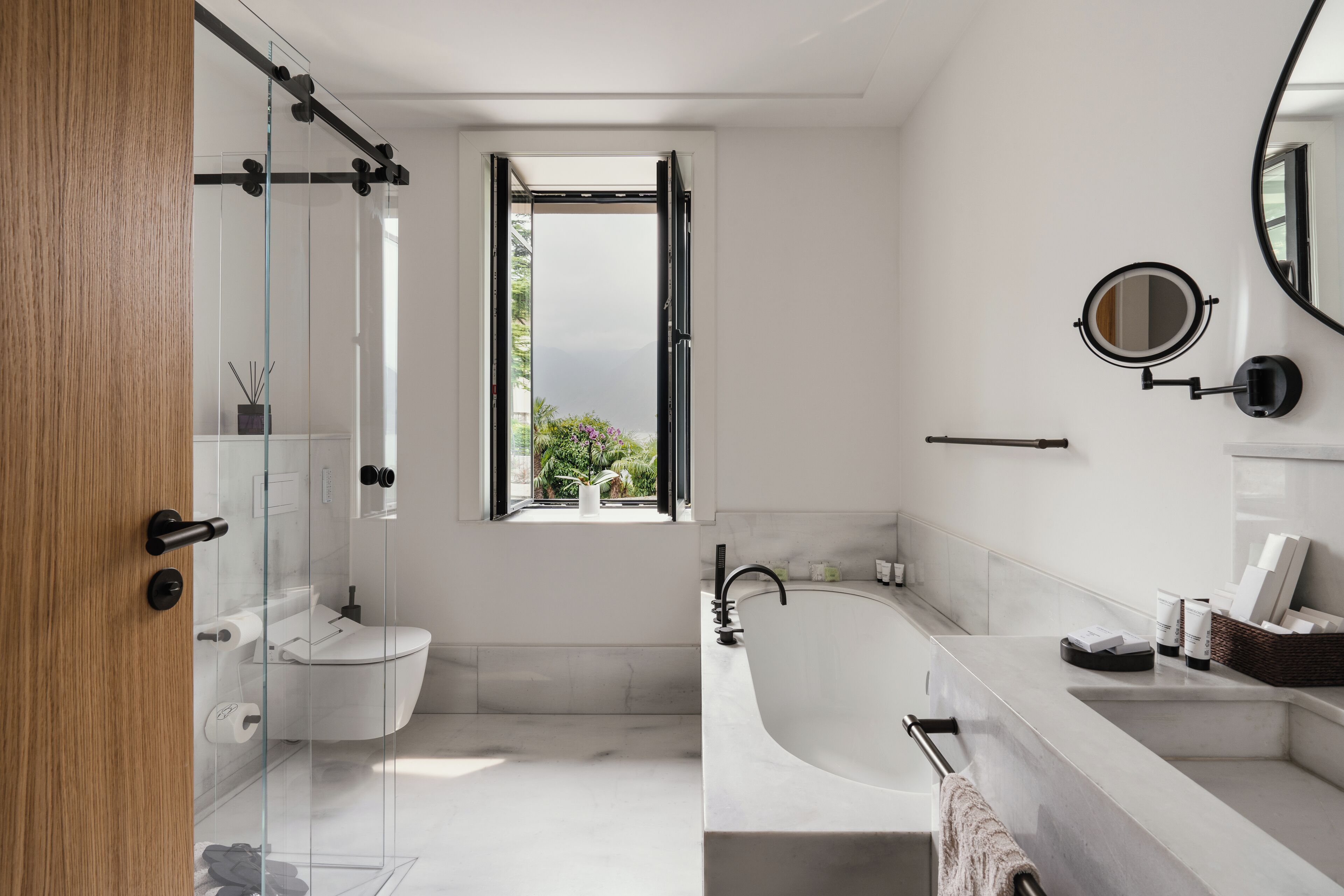 Un baño moderno con cabina de ducha de vidrio, inodoro, bañera independiente y tocador con espejo.