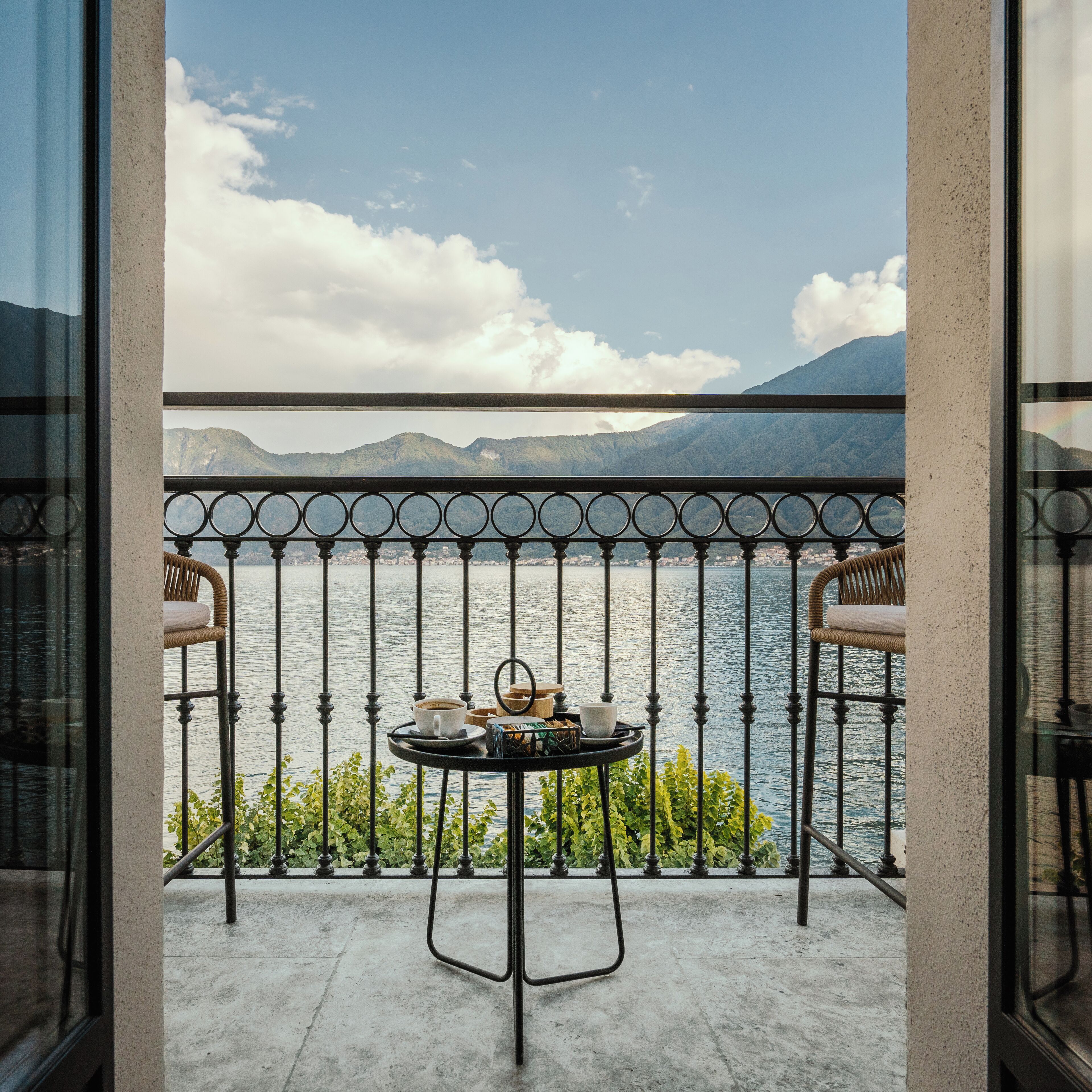 Ein Balkon mit Tisch für zwei Personen, mit Blick auf ein Gewässer und Berge.
