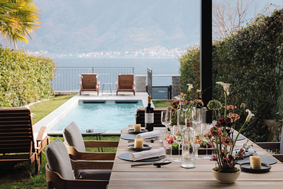 A dining table set for two with a view of a pool and mountains.