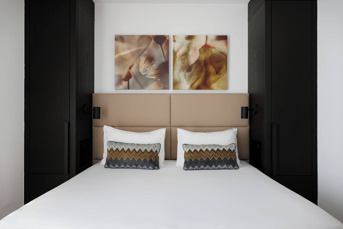 A bedroom with a bed, two pillows, a headboard, and two wall-mounted artworks.