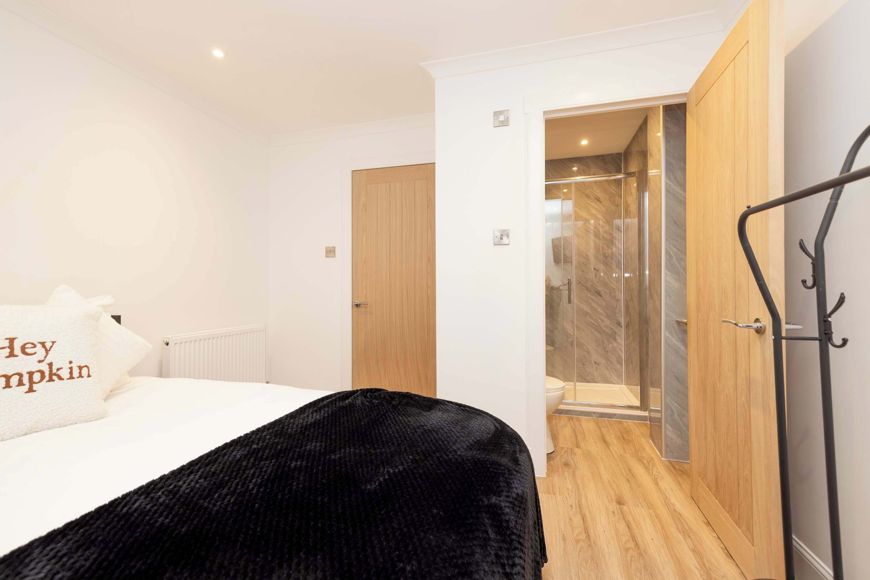 A hotel room with a bed, a black throw, a wooden door, and a shower area.