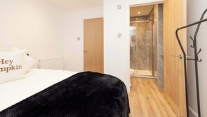Habitación de hotel con una cama, una manta negra, una puerta de madera y una zona de ducha.