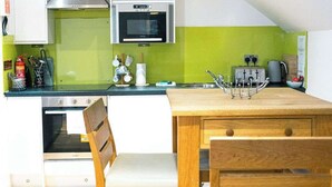 A compact kitchen with a microwave, stove, and green backsplash. There is a wooden table and two chairs.