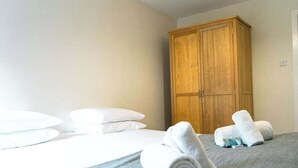 A hotel room with a bed, white pillows, a wooden wardrobe, and rolled towels on the bed.