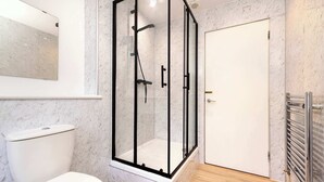 A modern bathroom with a glass-enclosed shower, a toilet, and a towel rack.