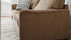 A beige sofa with a throw blanket and pillows, positioned in a room with white walls and a large window with blinds. - 2-bedroom apartment in Portland, ME with WiFi, AC. Enjoy your stay! (Portland)