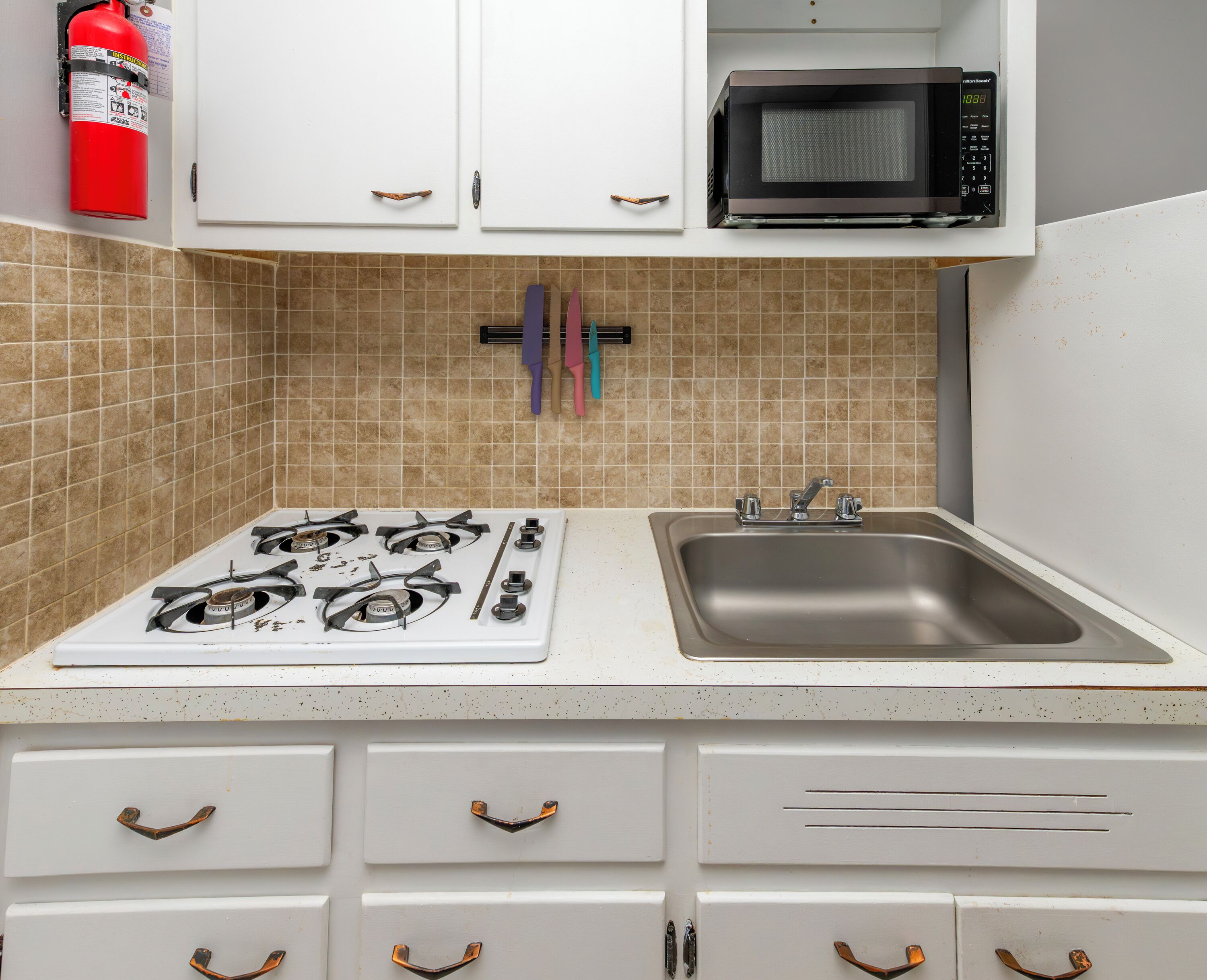 A kitchen with a gas stove, a sink, cabinets, a microwave, and a fire extinguisher.