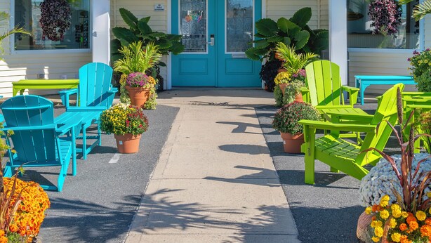 A hotel entrance with a blue door, outdoor seating with green chairs, and potted plants. - The Beach House at Drifting Sands (Beach Haven)