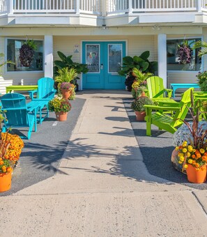 Ein Hotel mit Eingangstür in Blau, Sitzgelegenheiten im Freien mit grünen Stühlen und Kübelpflanzen.