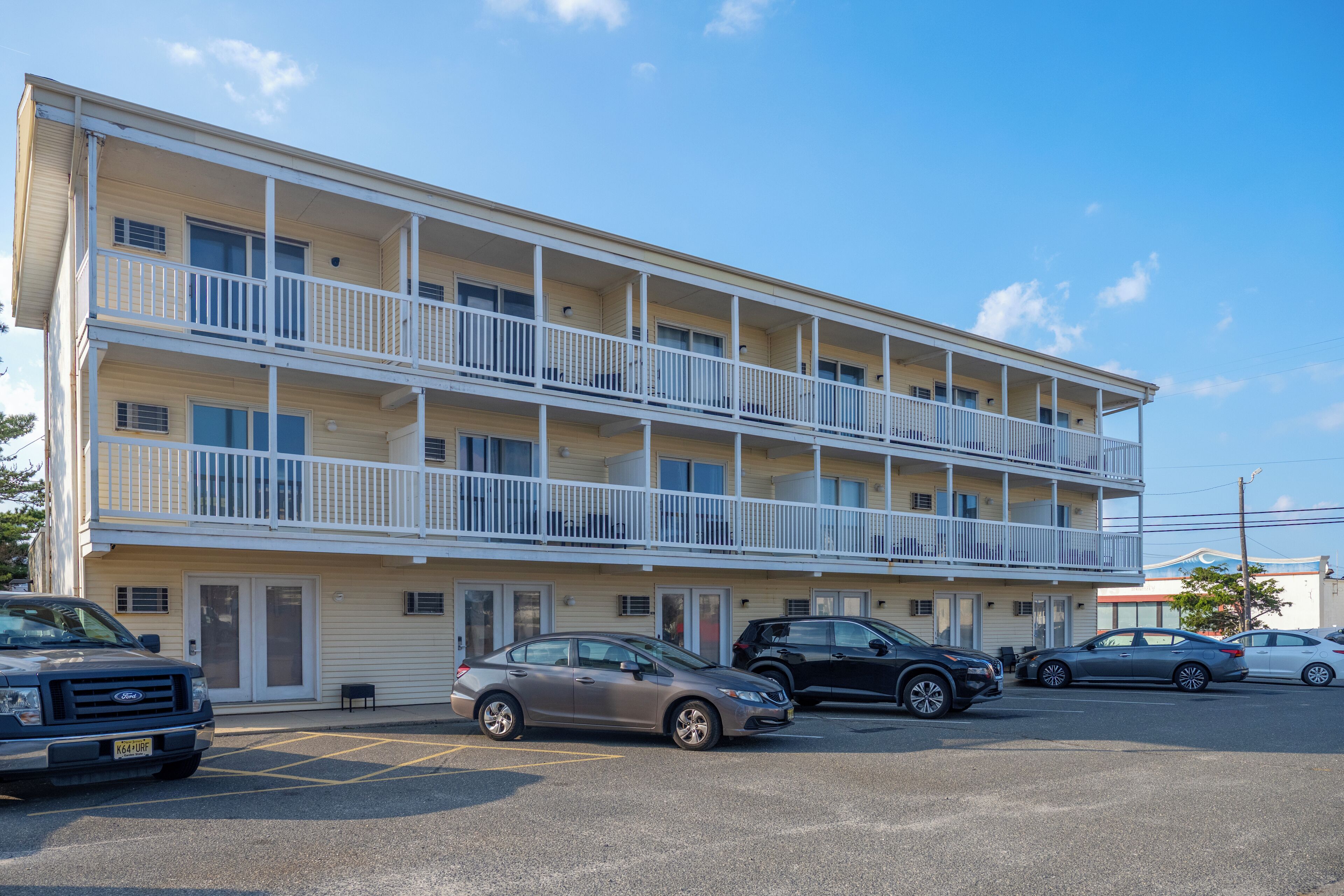 Un motel de varios pisos con balcones, estacionamiento y cielo despejado.
