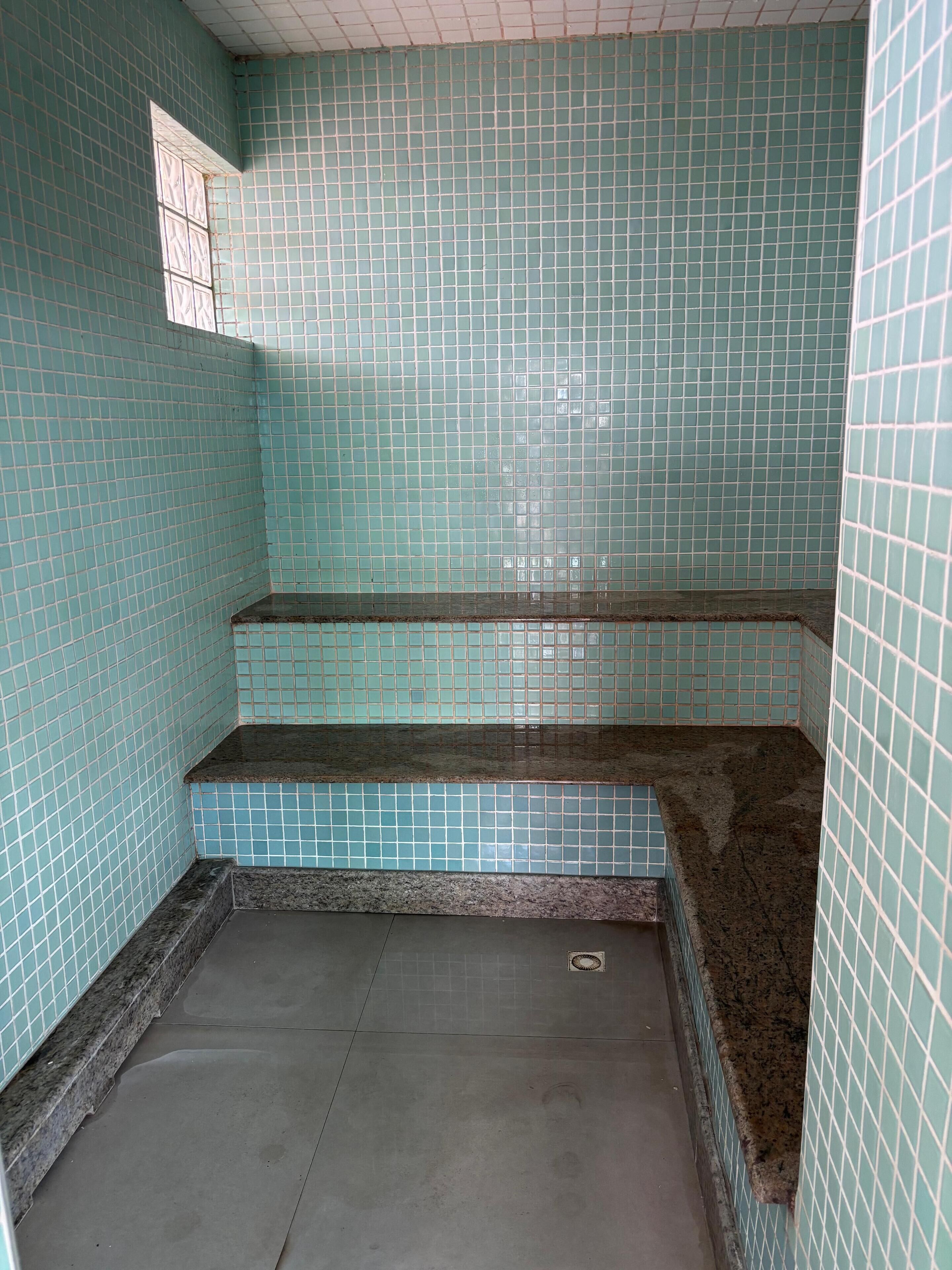 A tiled bathroom with a small window, a shower area, and a tiled floor.