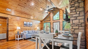 A wooden cabin interior with a dining table, chairs, a sofa, and a ceiling fan. - Couple's Escape | Hot Tub | Fire Pit (Broken Bow)