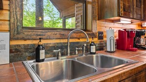 A kitchen with two stainless steel sinks, a wooden countertop, and a window overlooking greenery. - Couple's Escape | Hot Tub | Fire Pit (Broken Bow)
