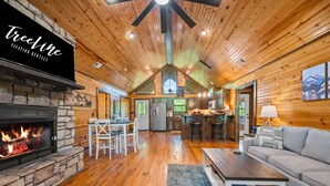 A spacious cabin interior with a stone fireplace, wooden floors, a dining area, and a kitchen. - Couple's Escape | Hot Tub | Fire Pit (Broken Bow)