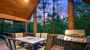 An outdoor deck with a table and chairs, a grill, and a view of the forest. - Couple's Escape | Hot Tub | Fire Pit (Broken Bow)