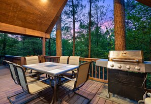 Una terraza exterior con mesa y sillas, una parrilla y vistas al bosque.