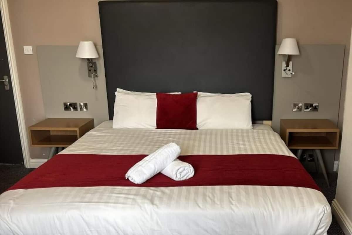 A hotel room with a large bed, two bedside tables, and two wall-mounted lamps.