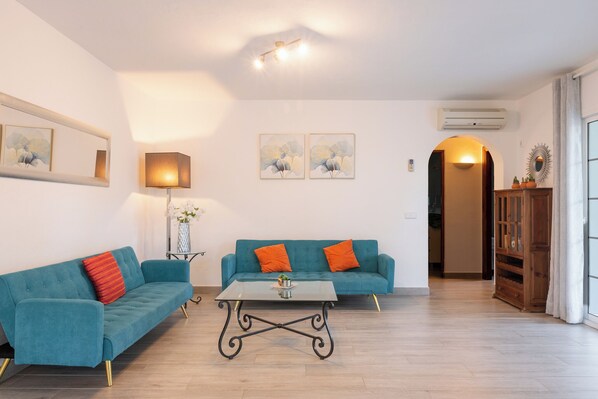 A living room with two teal sofas, a glass coffee table, and a lamp.