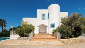 A white building with blue accents, a stone staircase, and a pool.