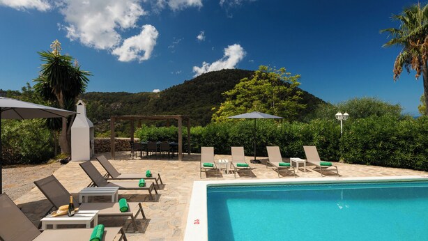 A poolside area with lounge chairs, a pool, and a view of a hill.