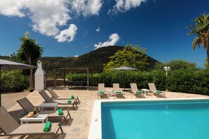 A poolside area with lounge chairs, a pool, and a view of a hill.