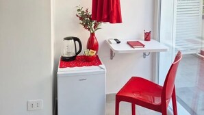 Ein gemütlicher Raum mit Küchenzeile, einem roten Sessel, einem kleinen Tisch, einem roten Kleid, das hängt, und einem Fenster mit Blick.