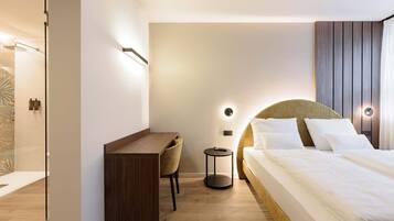 A modern hotel room with a bed, bedside table, chair, and a desk.