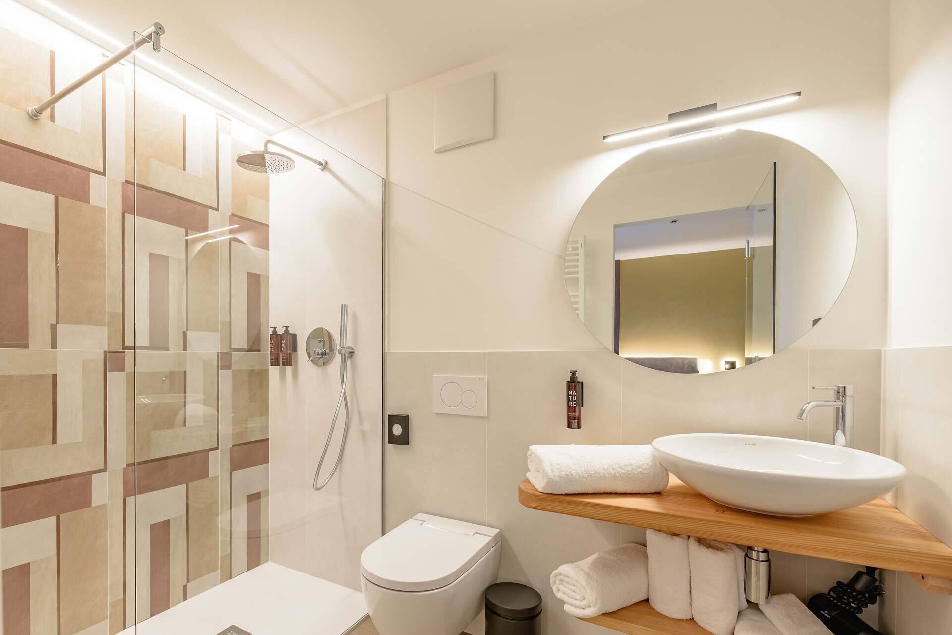 A modern bathroom with a glass shower enclosure, a white toilet, a sink with a wooden countertop, and a mirror.