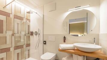 A modern bathroom with a glass shower enclosure, a white toilet, a sink with a wooden countertop, and a mirror.