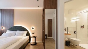 Ein modernes Hotelzimmer mit einem großen Bett, einem Nachttisch und einem Spiegel, der das Badezimmer reflektiert.