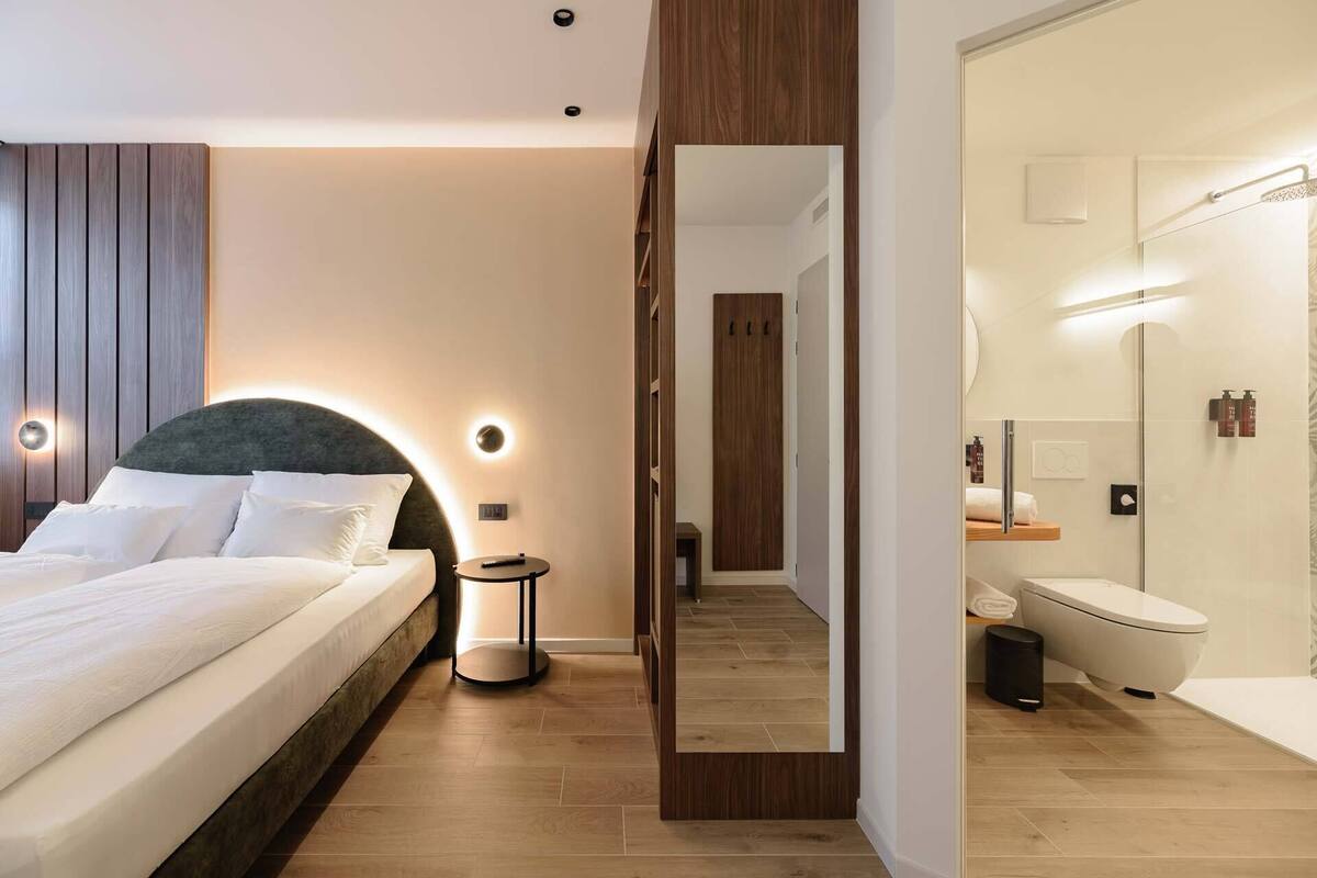 Une chambre d’hôtel moderne avec un grand lit, une table de chevet et un miroir qui reflète la salle de bain.