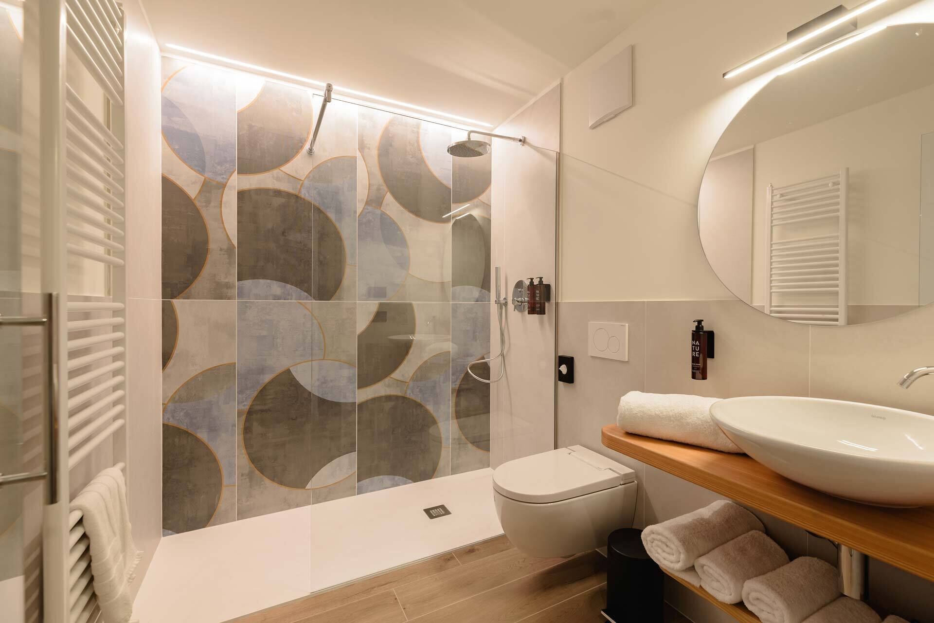 Un baño moderno con cabina de ducha de vidrio, inodoro blanco, lavamanos con encimera de madera y espejo sobre el lavamanos.