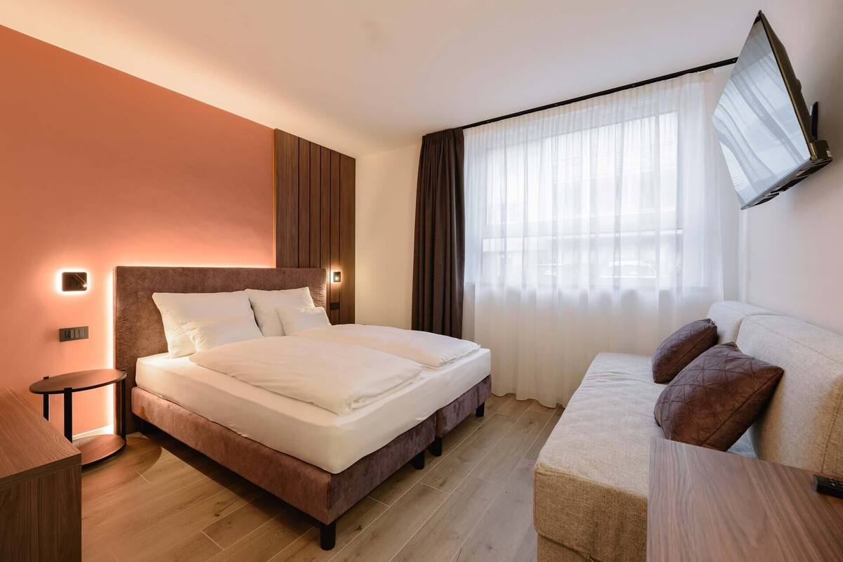 Une chambre d’hôtel avec un grand lit, un canapé, une petite table et un téléviseur fixé au mur.