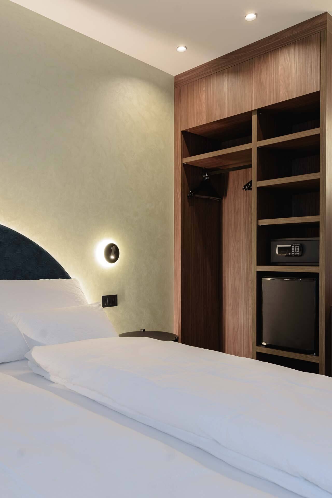 Une chambre d’hôtel avec un lit, une armoire intégrant un téléviseur et une lampe fixée au mur.