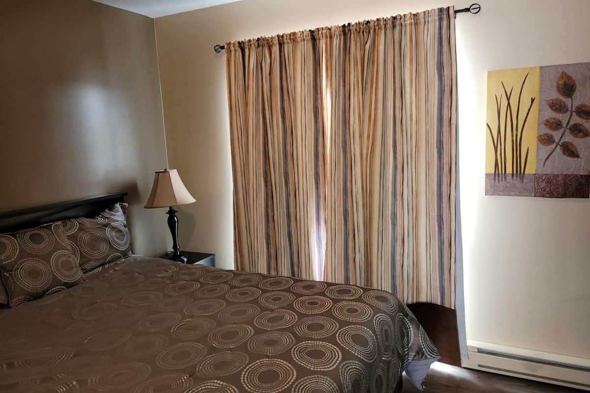 A bedroom with a bed, a nightstand, a lamp, a curtain, and a wall art piece.