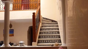 A living room with a patterned sofa, a staircase with geometric designs, and a view of a balcony with a wooden railing. - MARRAKECH RYAD ALL COMFORTS IN A RESIDENCE WITH 3 LARGE SWIMMING POOLS (Marrakech)