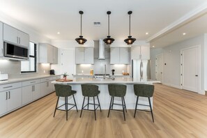 A modern kitchen with white cabinets, a central island, bar stools, and pendant lighting.