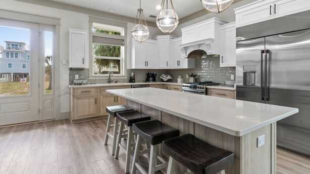 A modern kitchen with white cabinets, a large island with bar stools, stainless steel appliances, and pendant lighting.