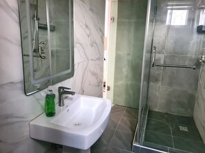 Une salle de bain avec un lavabo blanc, un miroir et une douche fermée par une paroi de verre.