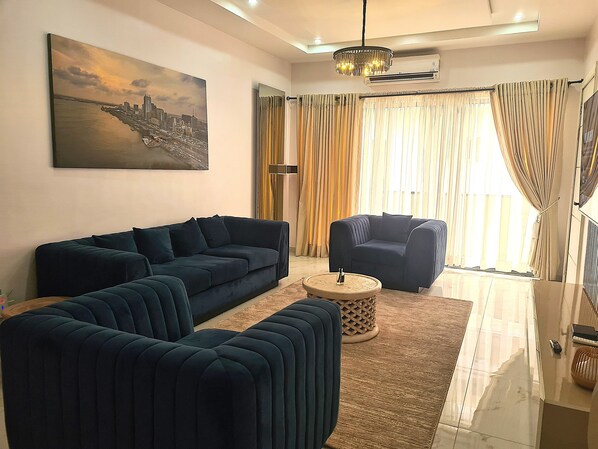 Una sala moderna con un sofá modular, una mesa de centro redonda y una pintura de un paisaje urbano en la pared.