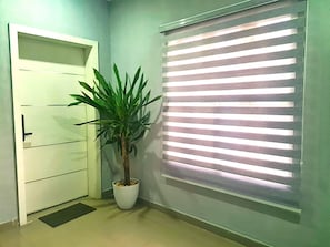 A hallway with a white door, a potted plant, and a window with horizontal blinds. - Lux 3BD/3BA Flat | Parkview Ikoyi | NG01 (Lagos)