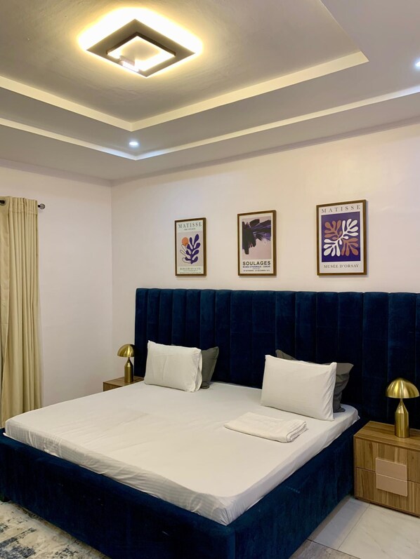 Une chambre à coucher moderne avec un grand lit, une tête de lit bleu foncé et deux tables de chevet avec des lampes.