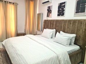 Habitación de hotel con una cama grande, cabecera, mesita de noche y aire acondicionado instalado en la pared.