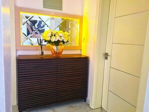 Une commode en bois foncé, surmontée d’un miroir qui reflète un motif géométrique sur le mur.
