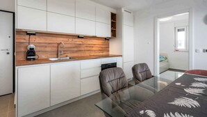 Een moderne keuken met witte kastjes, een houten aanrecht en een koffiezetapparaat. In de achtergrond staat een glazen tafel met twee stoelen en een bank.