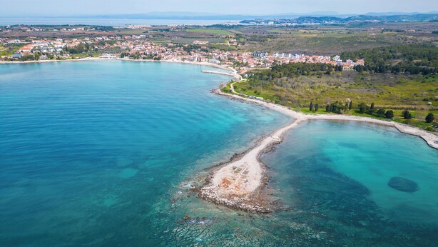 Luchtbeeld van een kustplaatsje met helder turquoise water, een zandstrand en een dichtbebouwd gebied.
